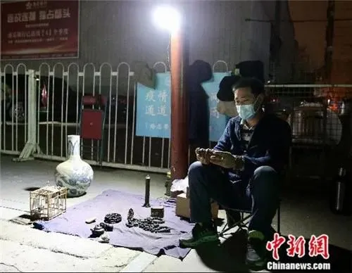 4月2日晚，魏根华在摊位前休息。由于小雨，他已把摊位上的部分货品收起。中新社易海菲 摄
