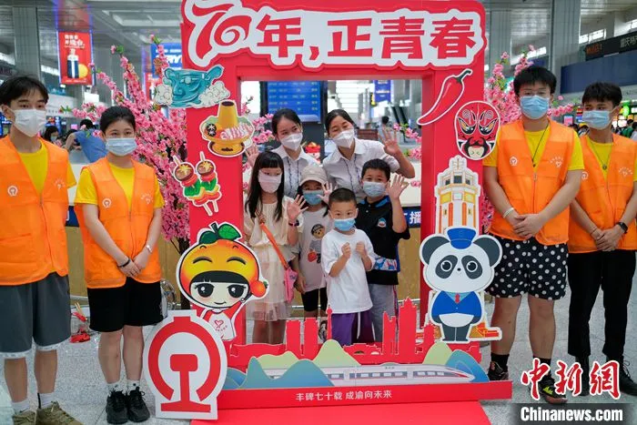 图为重庆北站候车大厅，旅客与铁路青年志愿者们在成渝铁路开通运营70周年的纪念展板前合影留念。 中新社记者 何蓬磊 摄