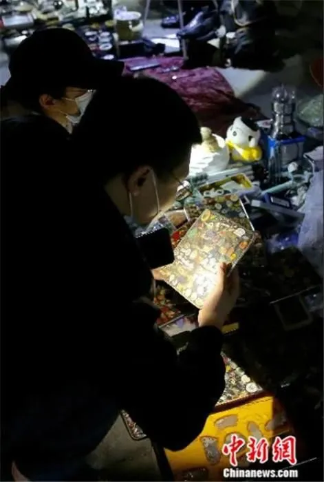 4月2日晚，一位买家在“鬼市”摊位前拿着手电仔细查看货品。中新社易海菲 摄