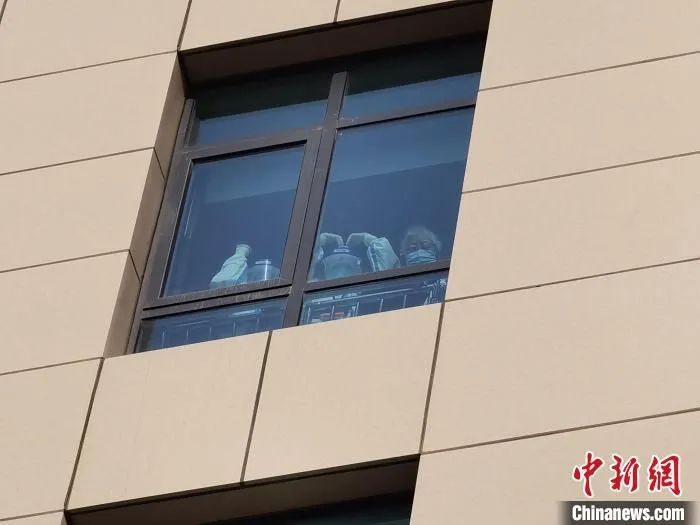图为封控区内，医护人员和居民站在窗户前向消杀人员们加油鼓劲。　祁增蓓 摄
