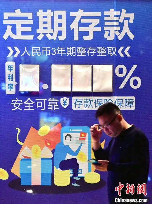 图为12月6日晚，福建福州，一市民从金融机构广告旁经过。 中新社记者 张斌 摄